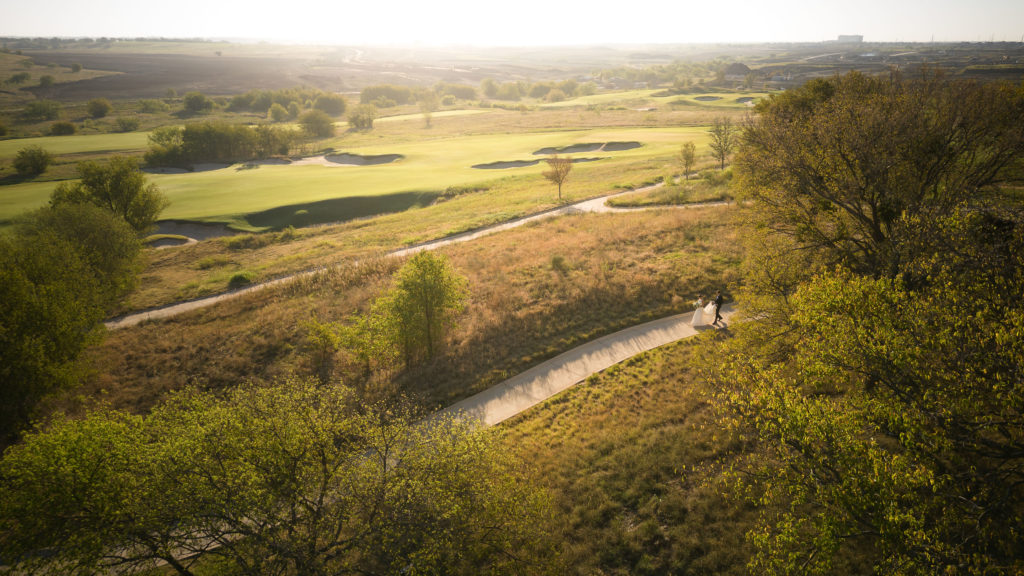 Aerial View photographed by a DJI Mini 3 drone of a bride and groom walking down the path at the New Omni Frisco PGA Hotel photographed by Carter Rose